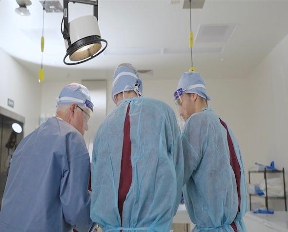 Three people in medical scrubs stand over an operating table. 